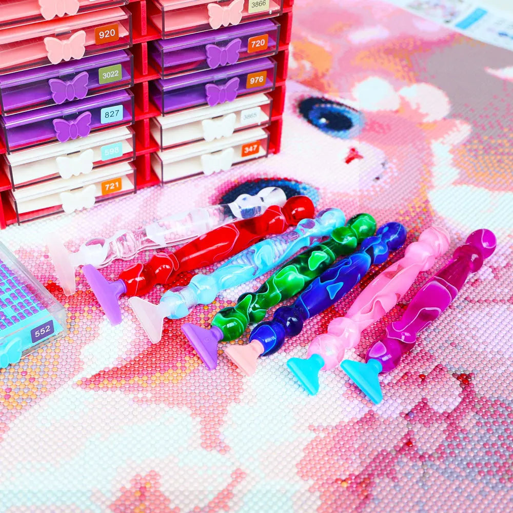 A collection of diamond art pens with various colored and shaped tips arranged in a red storage rack on a pink background.