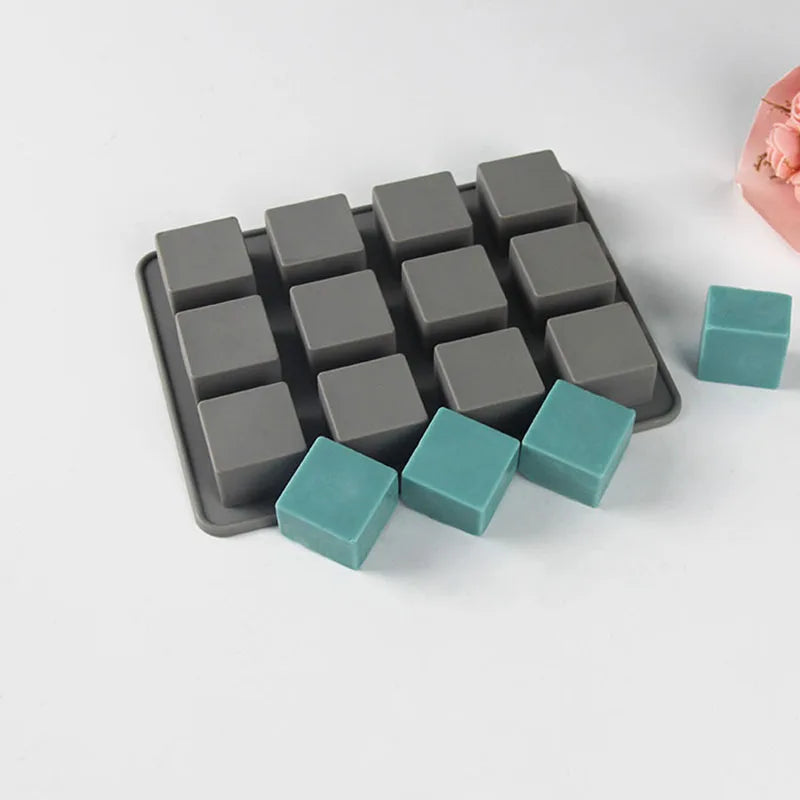 A silicone soap mold with 12 square cavities in various shades of gray and teal.