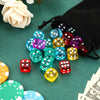 A collection of colorful acrylic 6-sided dice scattered on a green surface next to a black drawstring bag.