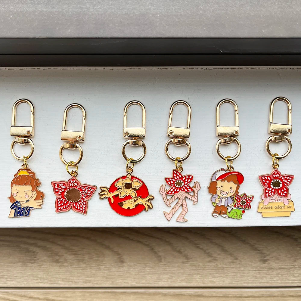 A set of six metal keychains featuring character pendants from Stranger Things, including a girl, a boy, and various figures.