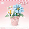 A pink potted flower arrangement made of building blocks featuring blue and white flowers.