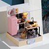 A clear acrylic display box featuring a miniature pink kitchen and living room setup for a DIY dollhouse kit.