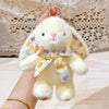 A fluffy white bunny plush toy with a floral bow charm is being held by a hand.