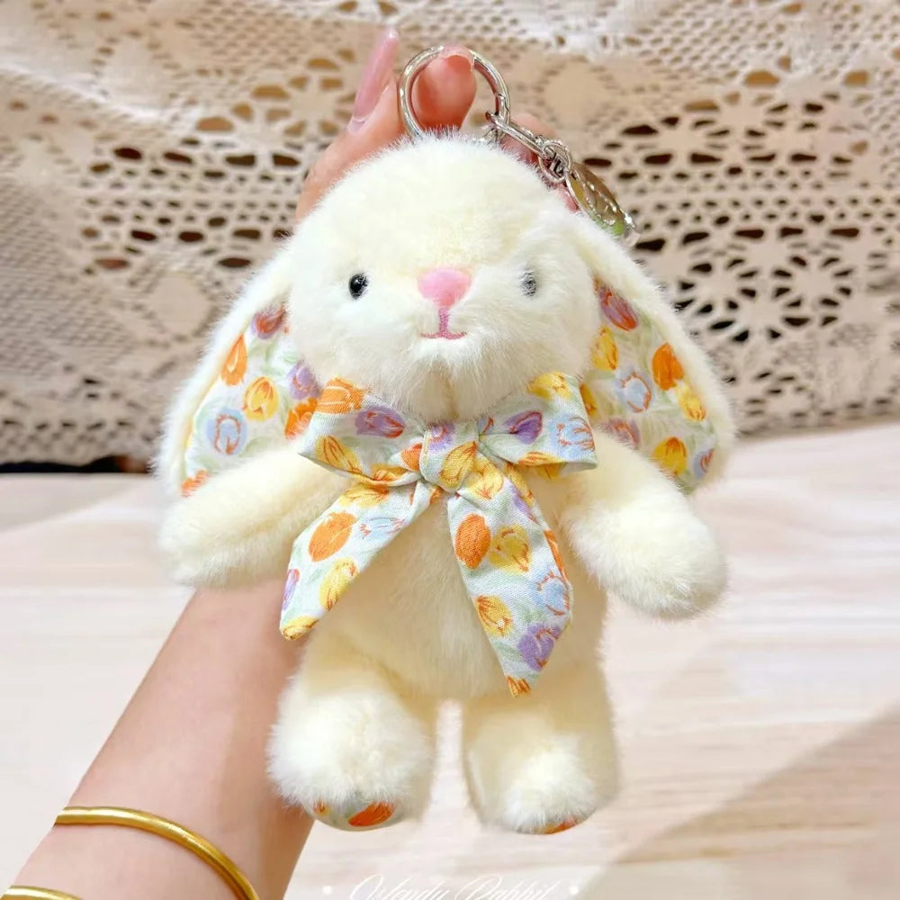 A fluffy white bunny plush toy with a floral bow charm is being held by a hand.