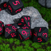A set of black polyhedral dice resting on a gray rock amidst green grass.