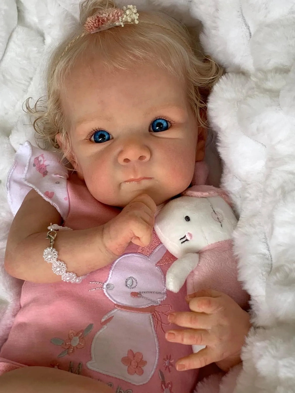 A close-up of an 18-inch lifelike reborn baby doll with hand-rooted hair wearing a pink outfit.
