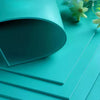 A stack of teal PVC carving blocks and rubber slabs displayed on a light surface.