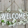 A wooden sign decorated with white flowers hangs on a weathered wooden background.