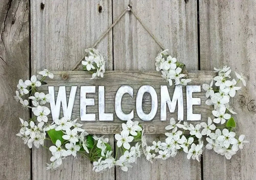 A wooden sign decorated with white flowers hangs on a weathered wooden background.
