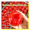 A hand holds a red watermelon slush squeeze ball next to a tray of similar red balls.