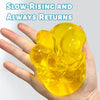 A hand holds a yellow honey cheese squishy stress ball, demonstrating its slow-rising and returning properties.