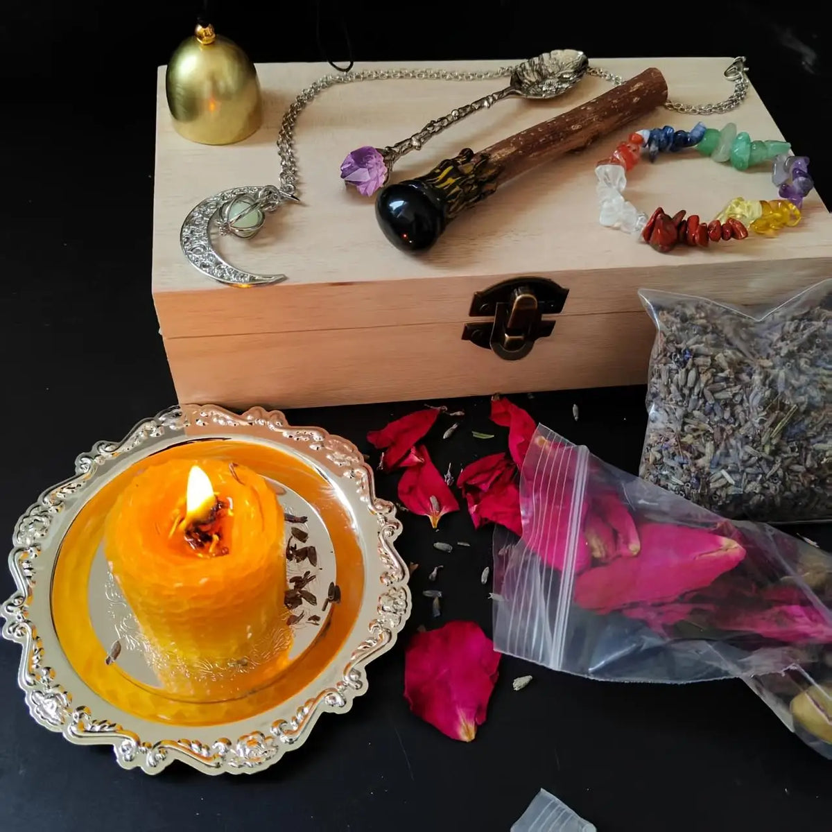 A witchcraft starter kit featuring a wooden box, crystals, herbs, and an orange candle on a silver plate.