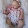 A newborn baby doll with hand-painted skin is lying on a white fluffy surface.