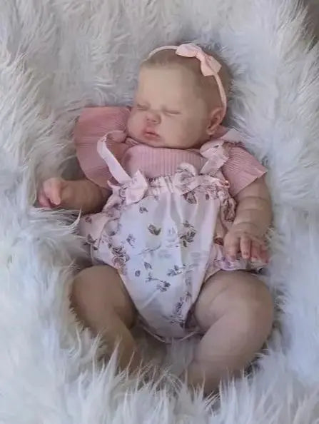 A newborn baby doll with hand-painted skin is lying on a white fluffy surface.