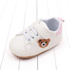 A pair of light beige baby sneakers featuring a cute brown bear design on the side.