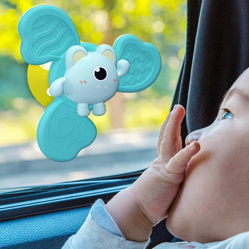 A light blue suction cup spinner bath toy shaped like an elephant is being held by a baby looking out of a car window.