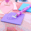A purple diamond painting clay block is being worked on with a pink and purple precision wax tool.
