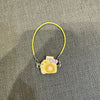 A yellow cord necklace with a small yellow camera charm and purple accents.