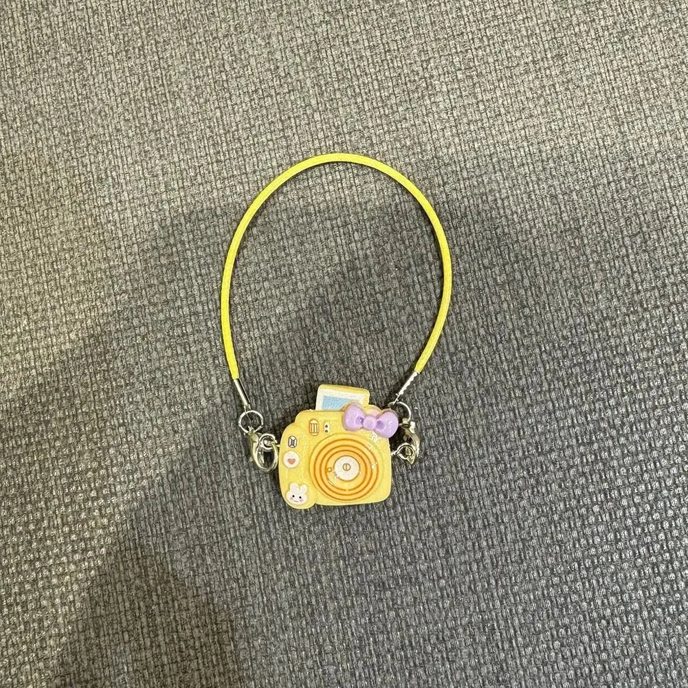 A yellow cord necklace with a small yellow camera charm and purple accents.