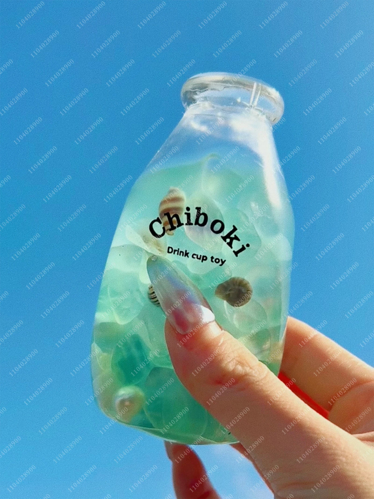 A hand holds a clear, light green bottle filled with liquid and a small, squishy toy inside.