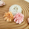 A silicone mold shaped like a carnation flower in peach and pink colors rests on a wooden surface.