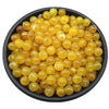 A pile of translucent yellow acrylic round beads for jewelry making in a black bowl.