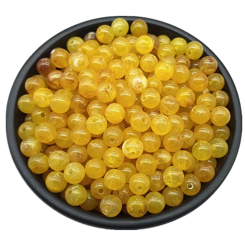 A pile of translucent yellow acrylic round beads for jewelry making in a black bowl.