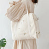 A light beige quilted diaper bag with subtle embroidery carried by a person wearing a matching outfit.