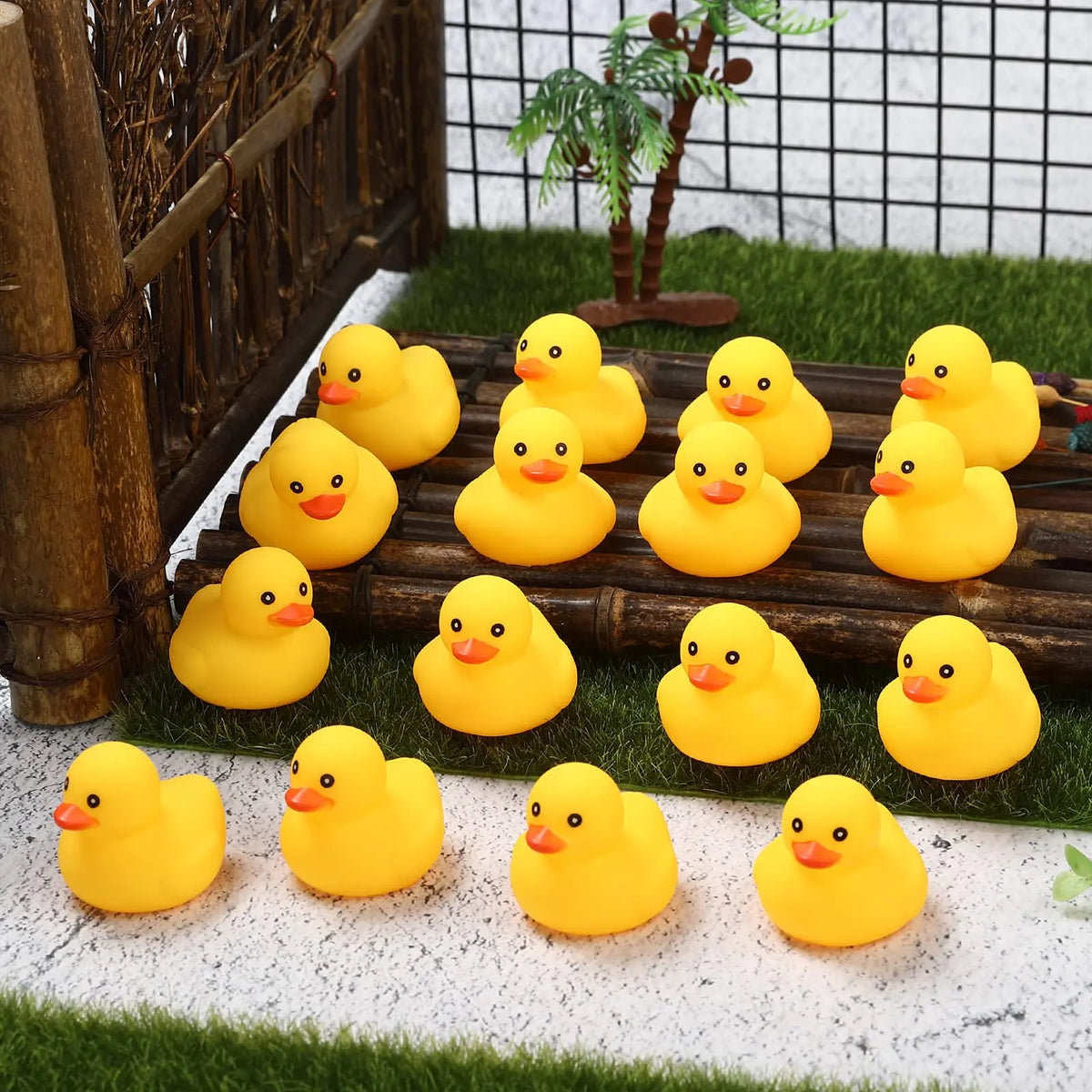 A set of yellow rubber ducks resting on green moss and white gravel with a wooden fence in the background.