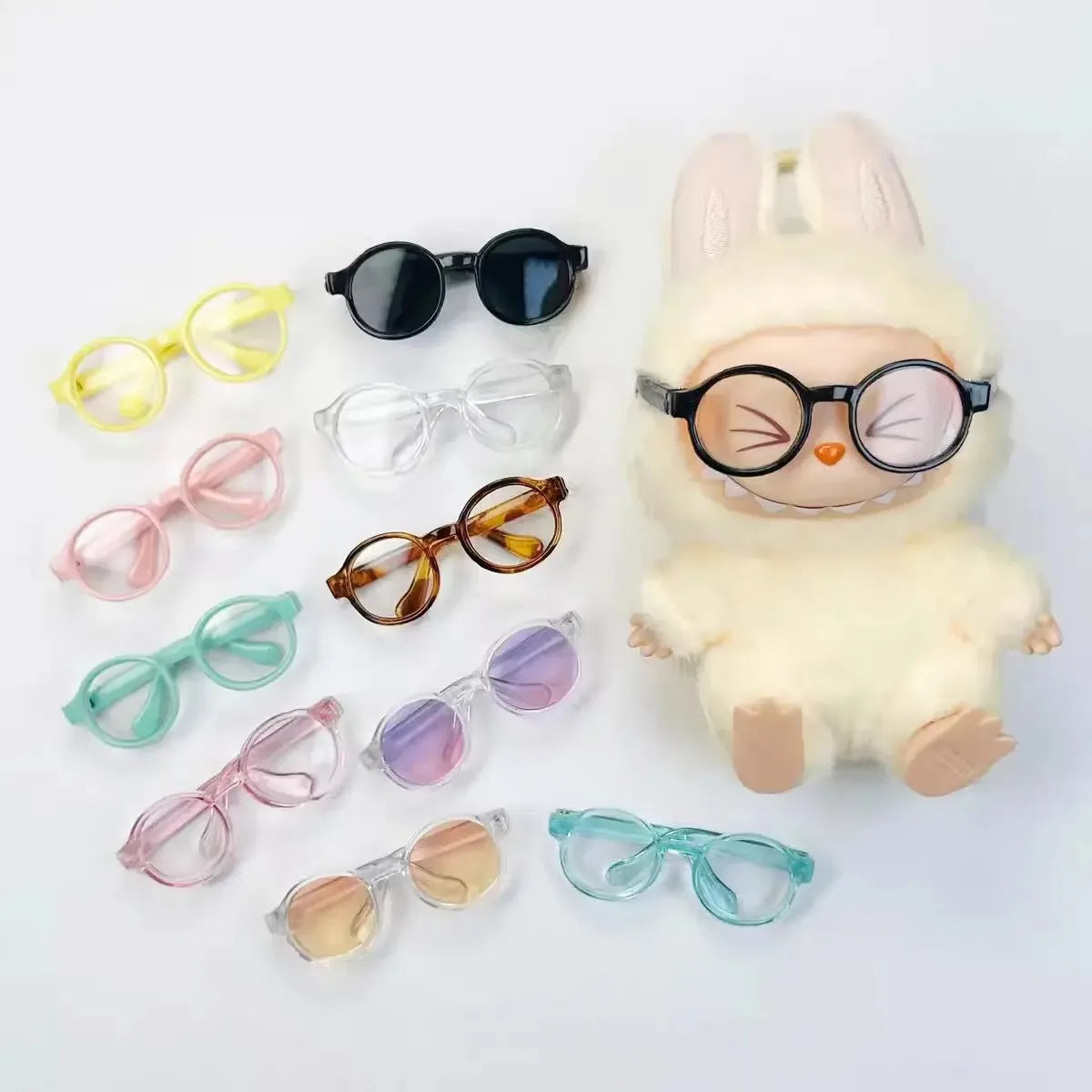 A collection of transparent doll glasses for BJD and Labubu dolls displayed next to a fluffy white rabbit figure.