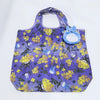 A purple fabric tote bag featuring a yellow floral pattern and a blue cartoon hippo plush toy.
