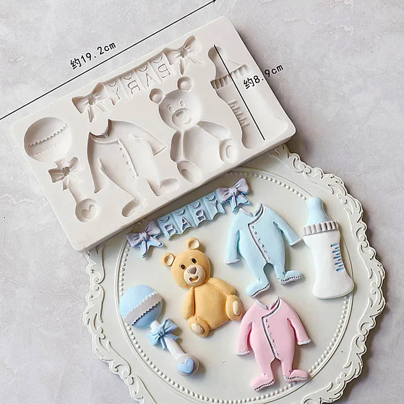 A set of white silicone baby-themed cake molds including a stroller, bottle, pacifier, and teddy bear shapes.