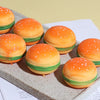 A collection of orange and green squishy stress balls shaped like burgers resting on a gray surface.