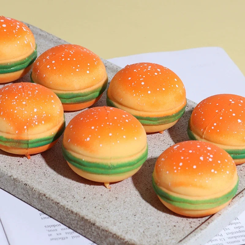 A collection of orange and green squishy stress balls shaped like burgers resting on a gray surface.