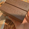 A hand holds a brown chocolate sensory squishy fidget toy box with the word CHOCOLATE embossed on it.