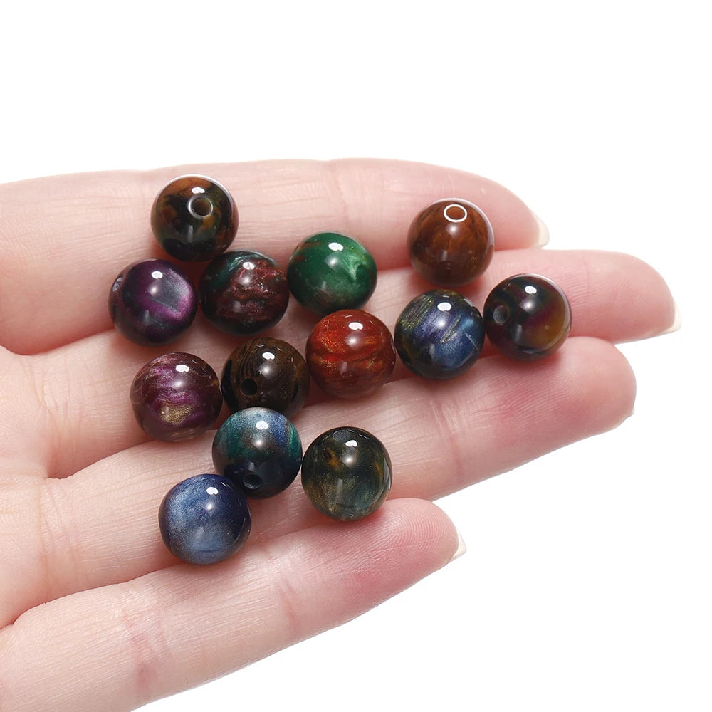 A hand holds several round, polished resin beads in various colors including purple, green, brown, and blue.