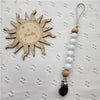 A wooden sun-shaped bead pacifier clip with a silicone teether on a leather cord.
