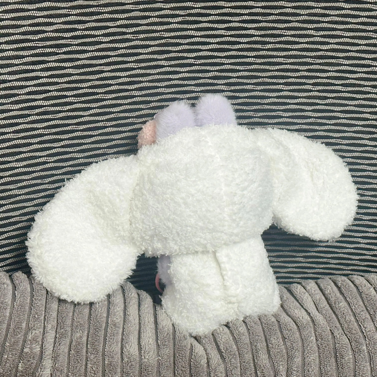 A white, fluffy rabbit costume with pink ears is displayed against a striped background.