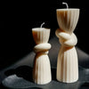 Two ivory silicone candle molds shaped like twisted ribbons stand on a dark surface.