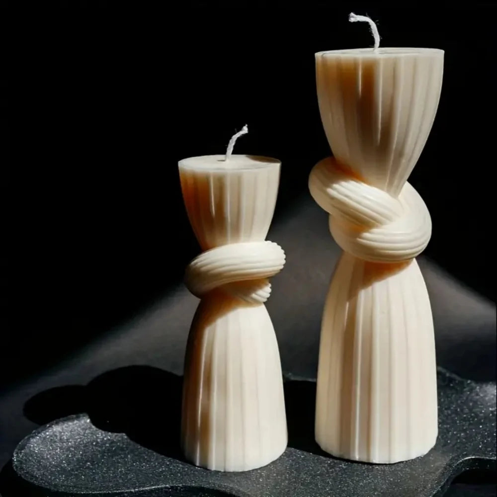 Two ivory silicone candle molds shaped like twisted ribbons stand on a dark surface.