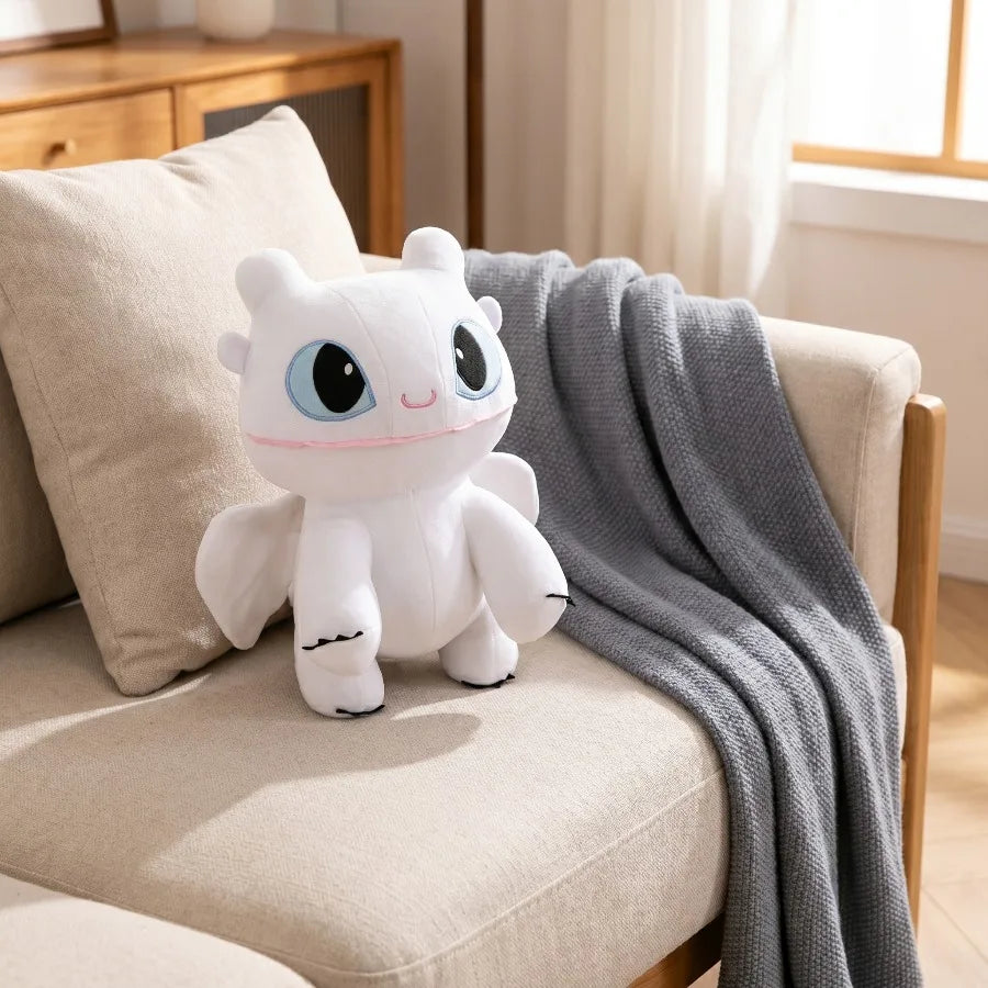 A white cartoon dragon plush toy resting on a beige sofa next to a gray blanket.
