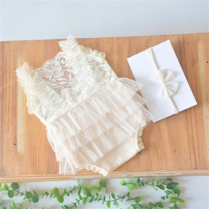 A cream lace baby romper with ruffled tiers and a matching white headband displayed on a wooden board.