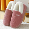 Pair of pink knitted slippers with white faux fur lining resting on a white surface.