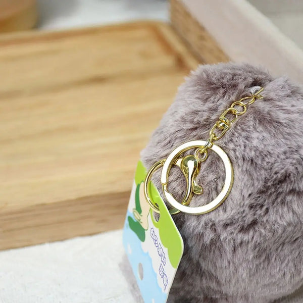 A fluffy gray hedgehog keychain with a gold-colored ring attached to a green tag.