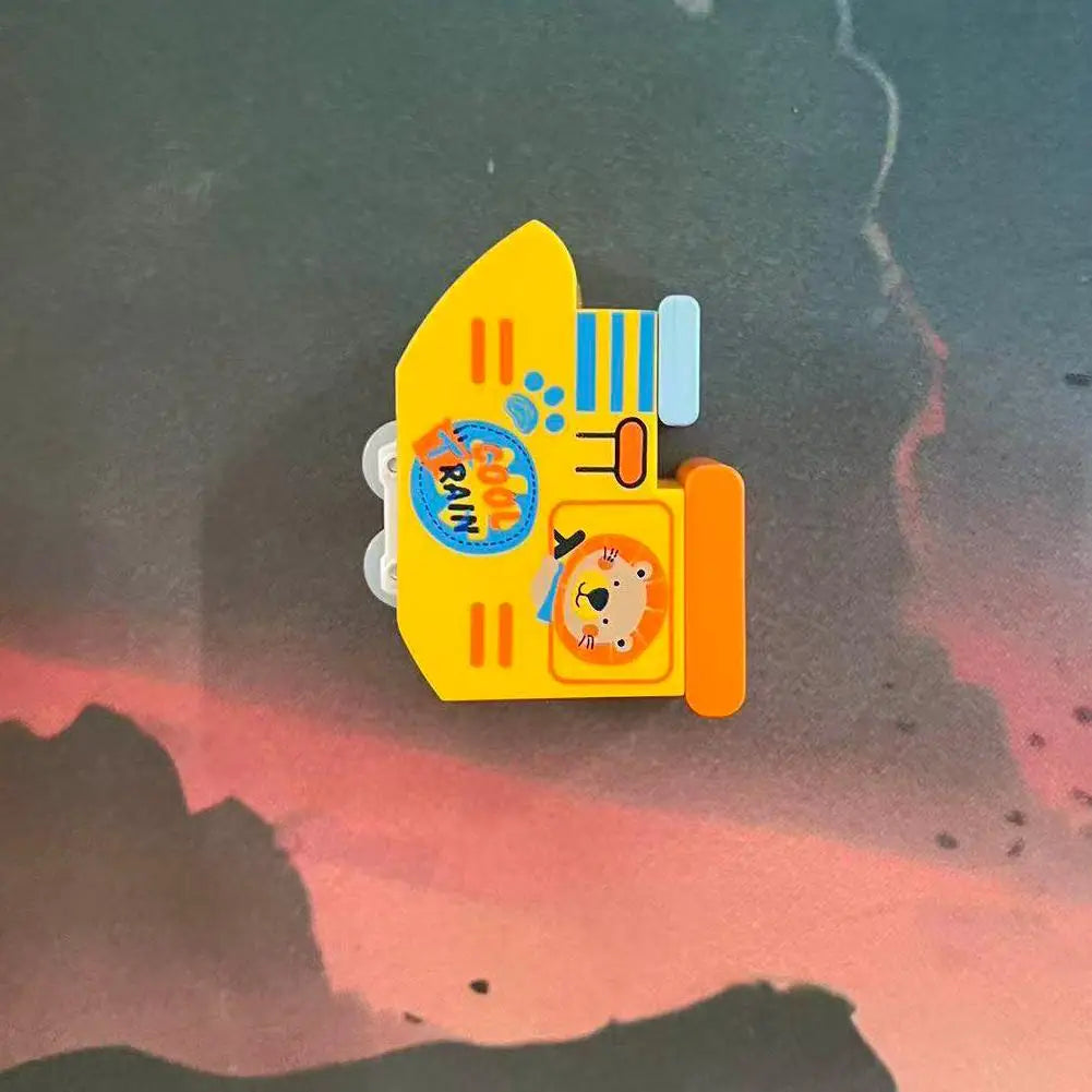 A yellow anti-gravity magnetic mini train toy with blue stripes and a bear face is shown against a pink sunset background.