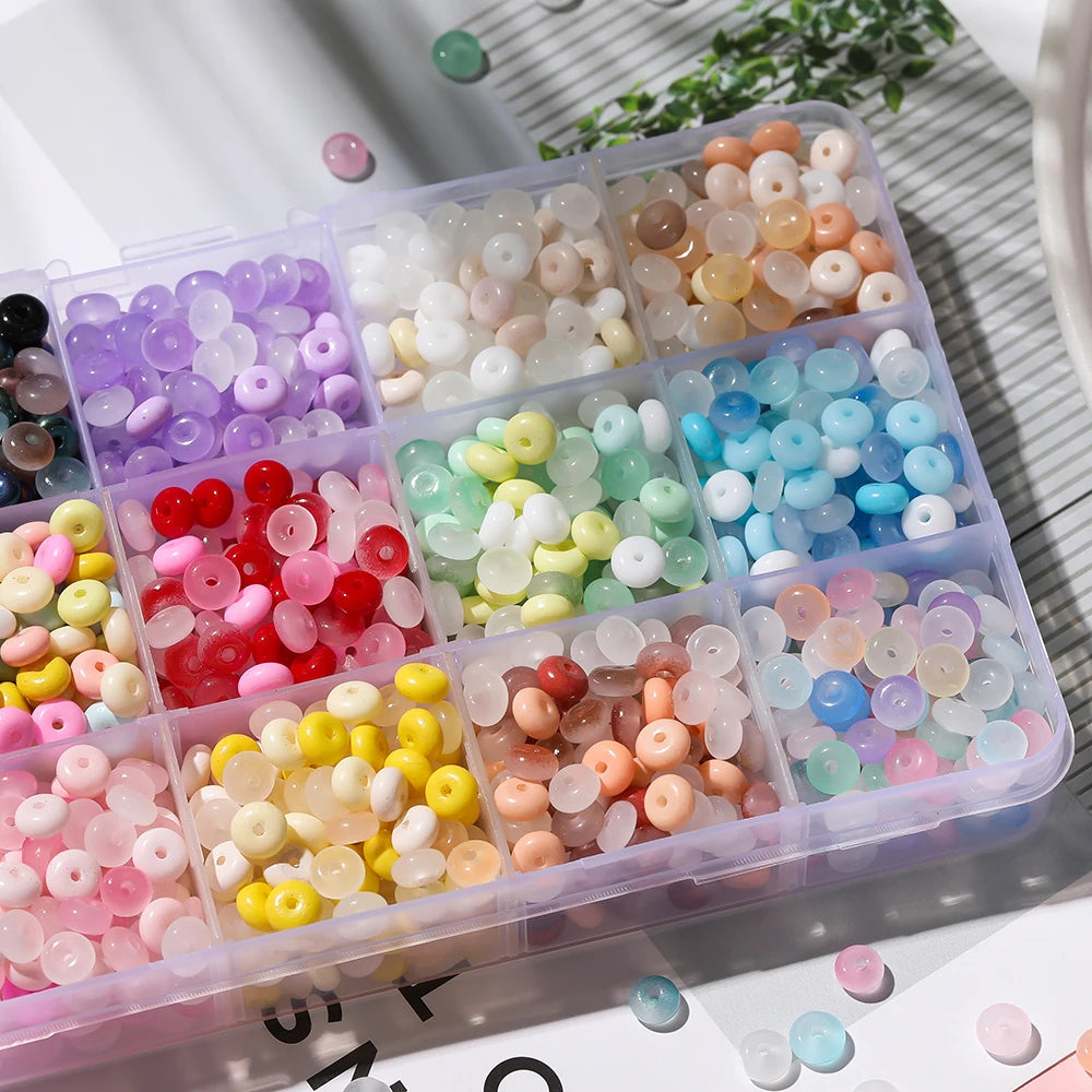 A clear plastic container filled with various colored glass spacer beads including purple, white, pink, red, yellow, and blue