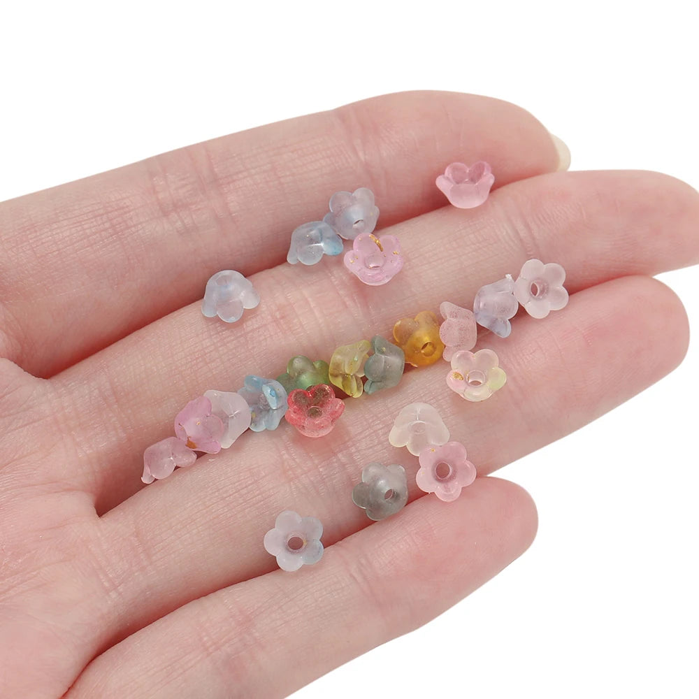 A hand holds a set of 50 gradient bellflower acrylic beads in various pastel colors for jewelry making