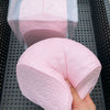A hand holds a pink squishy toy shaped like a loaf of bread, with a clear plastic container in the background.