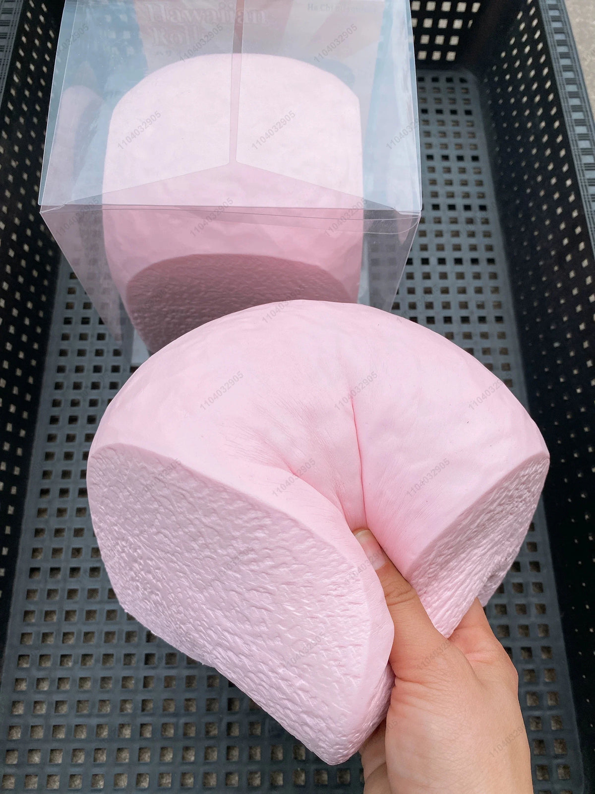 A hand holds a pink squishy toy shaped like a loaf of bread, with a clear plastic container in the background.