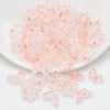 A pile of small, translucent pink glass butterfly beads for jewelry making.